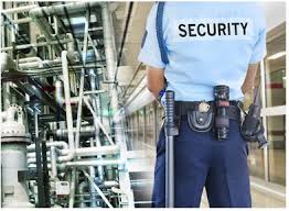 "The image shows a close-up shot of a security guard wearing a light blue uniform shirt with the word 'SECURITY' printed in white letters on the left breast. The guard appears to be indoors, possibly in a commercial setting, with a blurred background. The focus is on the text and the guard's uniform."